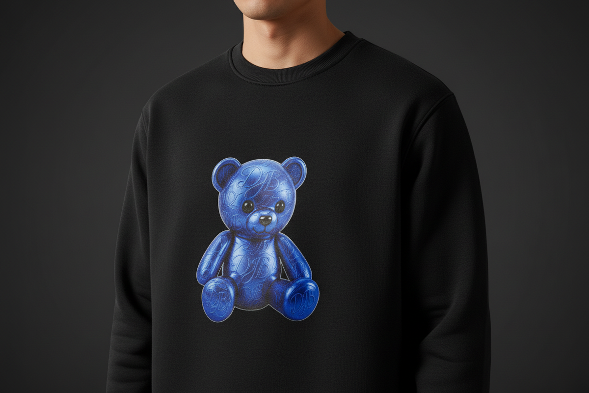 Close-up of the DJB Teddy heavyweight crewneck showing the blue teddy print, fleece texture, stitching, and ribbed cuff
